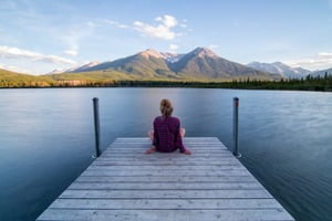 Frau sitzt am See und blickt auf die Berge