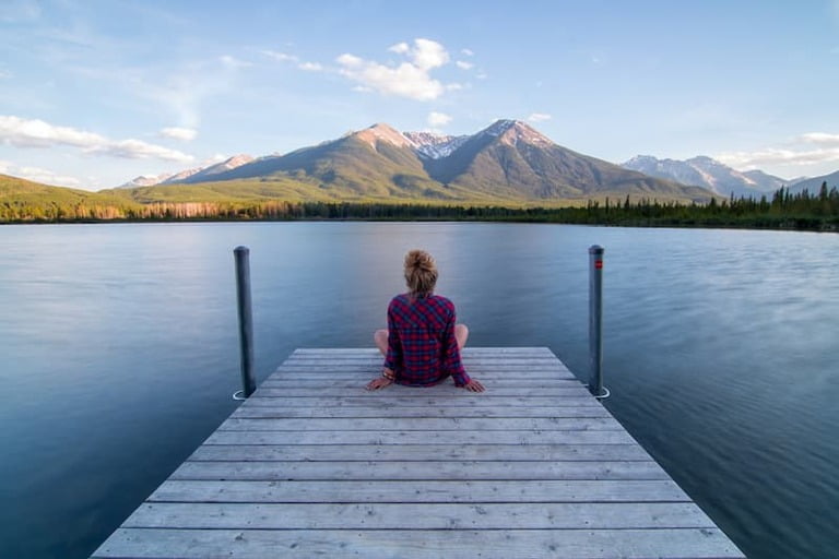 Frau sitzt am See und blickt auf die Berge